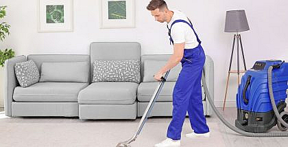 A professional cleaner using a vacuum on a carpet in a living room, representing carpet cleaning in Dubai.