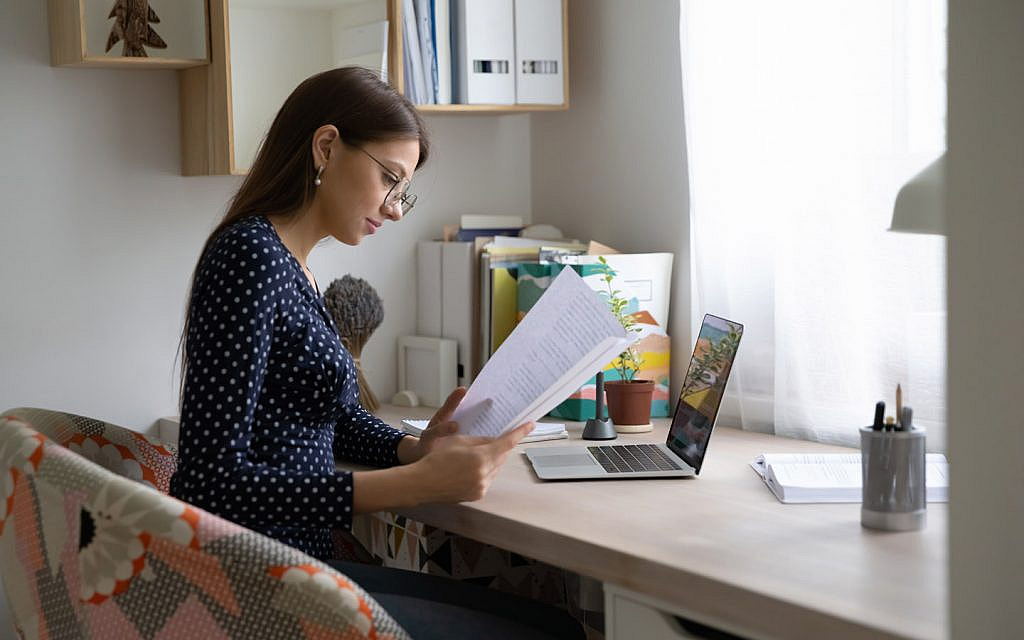 سيدة تحمل أوراقاً أثناء عملها على الحاسوب المحمول