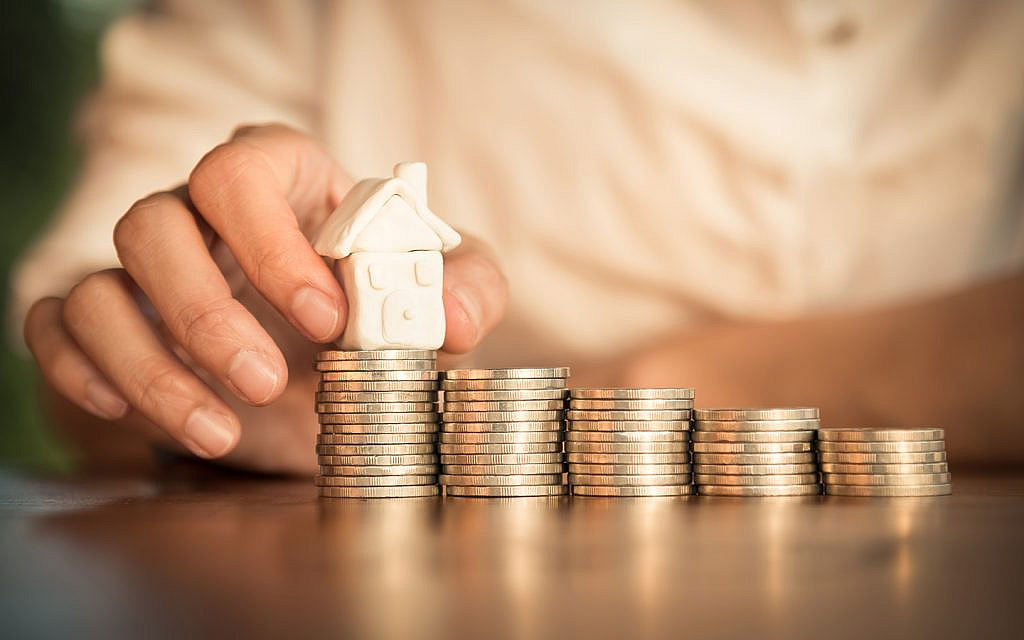 شخص يضع مجسم منزل فوق نقود معدنية