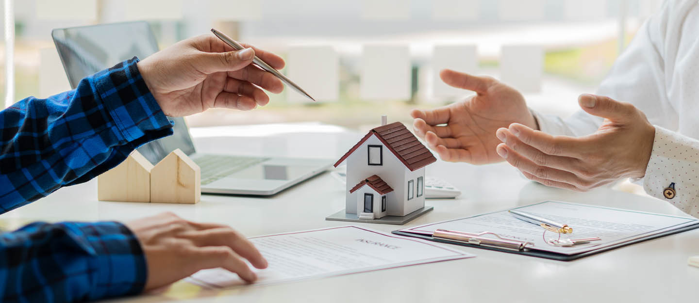 أشخاص يتفاوضون وبينهم مجسم منزل وأوراق