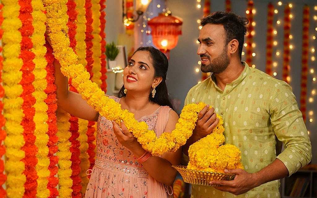 a couple decorating home with marigold flowers for diwali