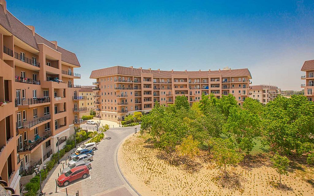 مجمعات سكنية حول مساحة خضراء مزروعة ومواقف اصطفاف للسيارات 