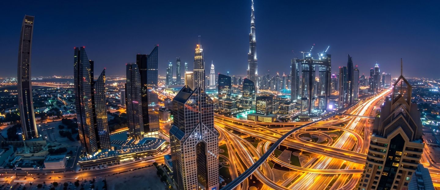 Aerial night view of Dubai skyline, Burj Khalifa, and intricate overpasses.
