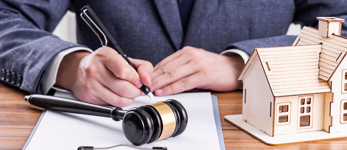 شخص يكتب على ورقة وبجانبه مطرقة ومجسم بيت