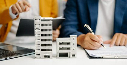 شخص يكتب على أوراق وامرأة تمسك بأوراق وتؤشر على مجسمات مباني