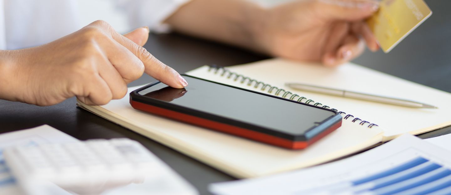 Close-up of a person holding a credit card in one hand while tapping the screen of a smartphone