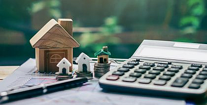قطع نقدية بجانب مجسم منزل وآلة حاسبة