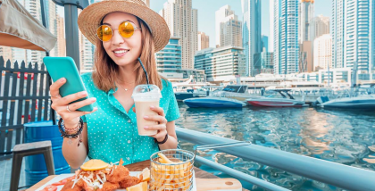 فتاة تستخدم الهاتف أثناء جلوسها في إحدى مطاعم منطقة دبي مارينا