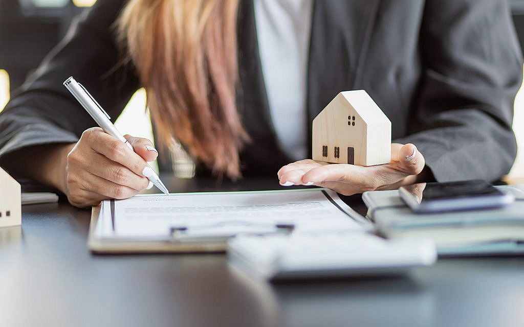 امرأة تمسك بمجسم منزل وتوقع على أوراق باليد الأخرى 