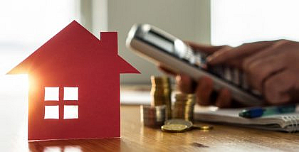 مجسم منزل وعملات نقدية وشخص يمسك آلة حاسبة