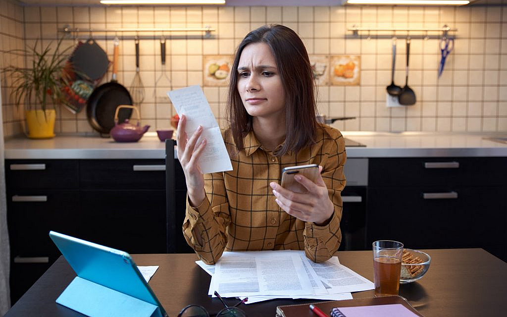 امرأة تمسك هاتفًا وفاتورة أمام تابلت