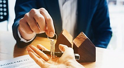 مجسمات منازل وشخص يسلم مفتاح منزل لآخر