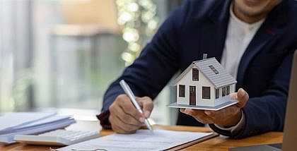 شخص يوقع ويمسك بيده الأخرى مجسم منزل