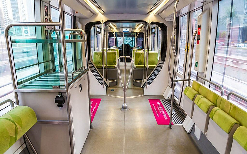 An inside view of a Dubai Metro train showing a clean, modern interior with green seats, handrails and spacious walkways.