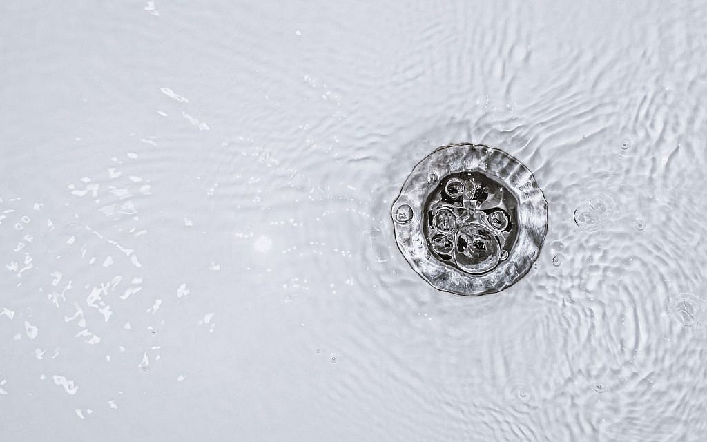 Slow-draining water in a white bathroom sink indicates a plumbing issue with water pooling around the drain.