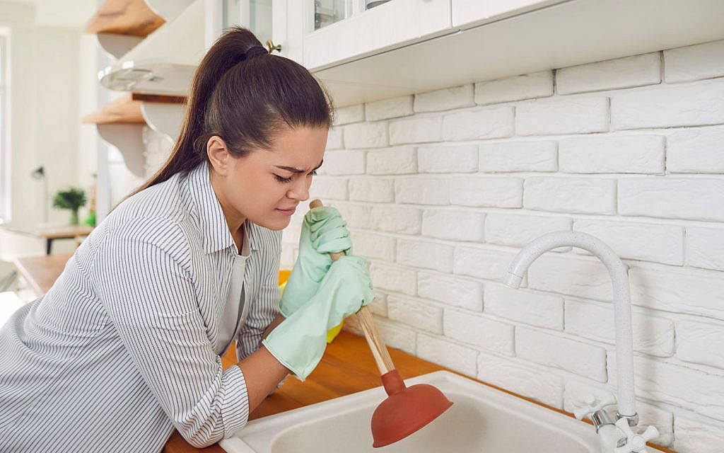 A woman is looking concerned while using a plunger on a sink, trying to fix a drainage problem.