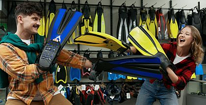 Man and woman playfully holding swimming fins in a swimming pool supply shop in Abu Dhabi, surrounded by displays of fins.