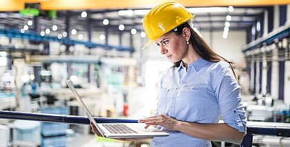 Woman in a hard hat using a laptop in an industrial facility, representing Facilities Management Companies in Dubai