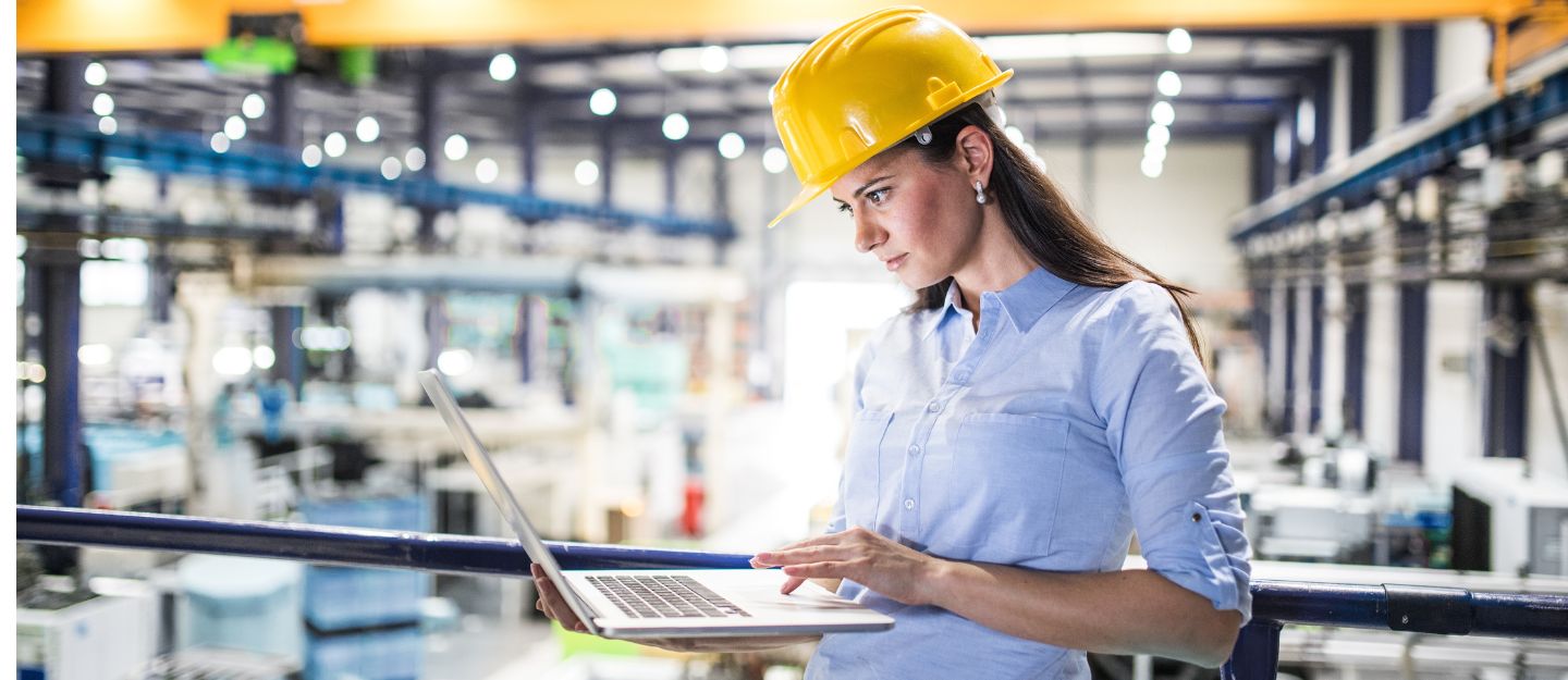 Woman in a hard hat using a laptop in an industrial facility, representing Facilities Management Companies in Dubai