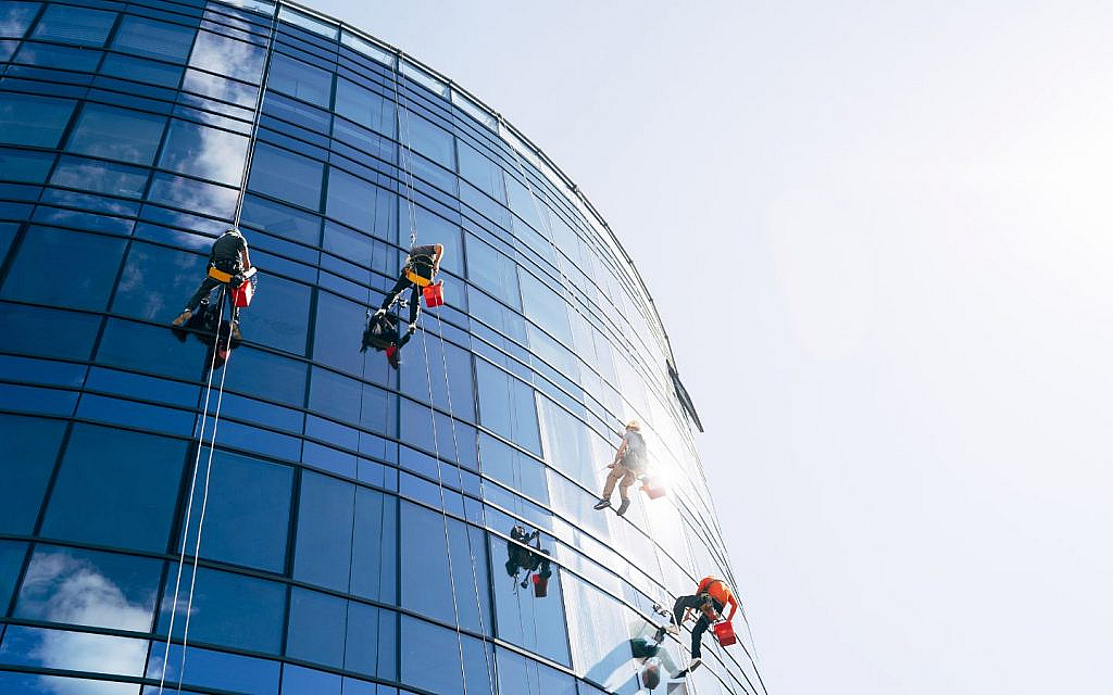 Workers are cleaning the exterior windows of a modern high-rise building.
