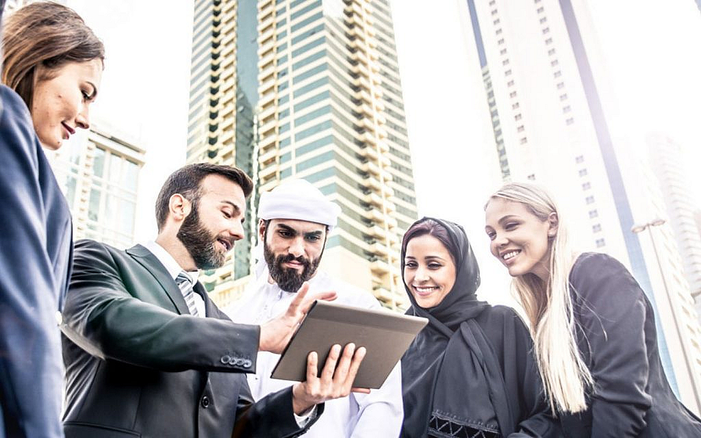 Group of diverse business professionals, looking at a tablet with tall buildings in the background.