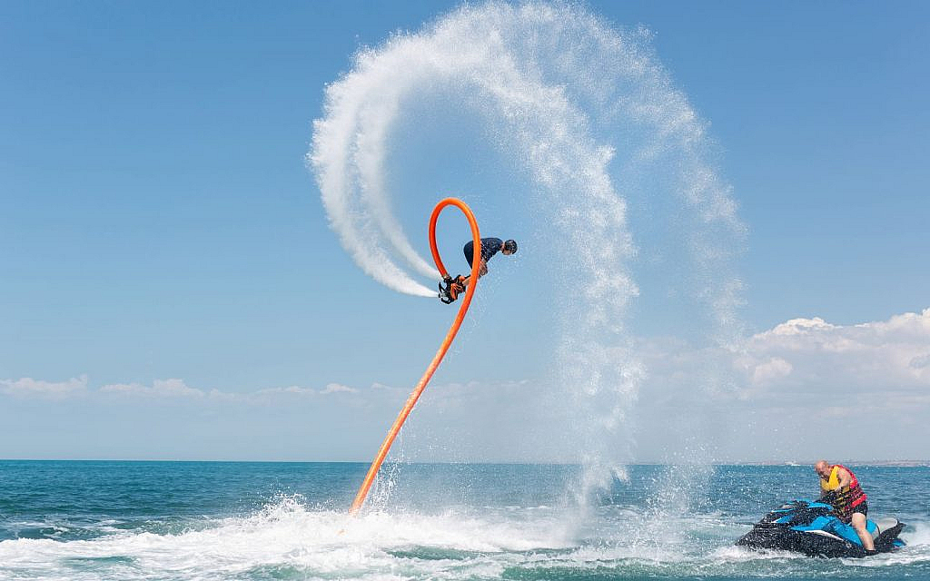 A person on a flyboard performing aerial manoeuvres, with water jets propelling them into the air over the ocean