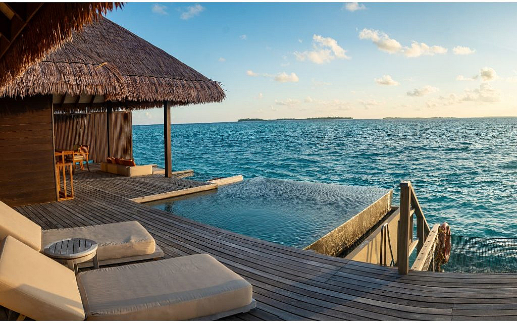 Overwater villa with a thatched roof, private infinity pool and lounge area overlooking the ocean.