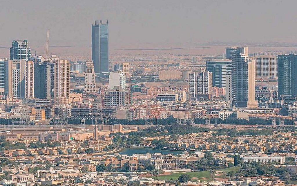 Aerial view of Jumeirah Village Circle with villas and a lake in the foreground and the Dubai skyline in the distance.