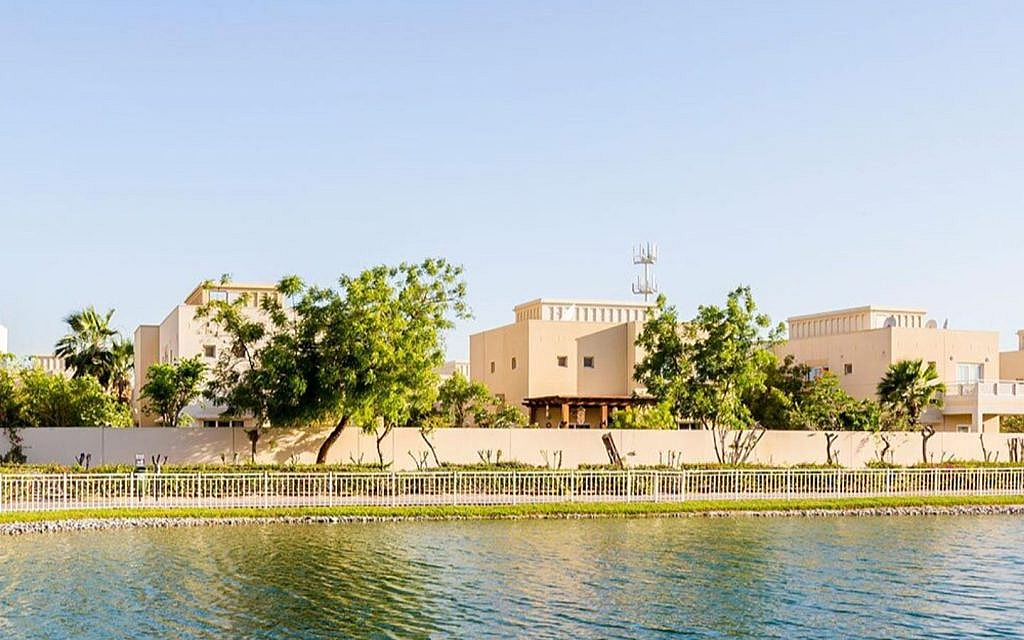 Villas along a calm lake or canal in a planned community, with green trees and a clear sky.