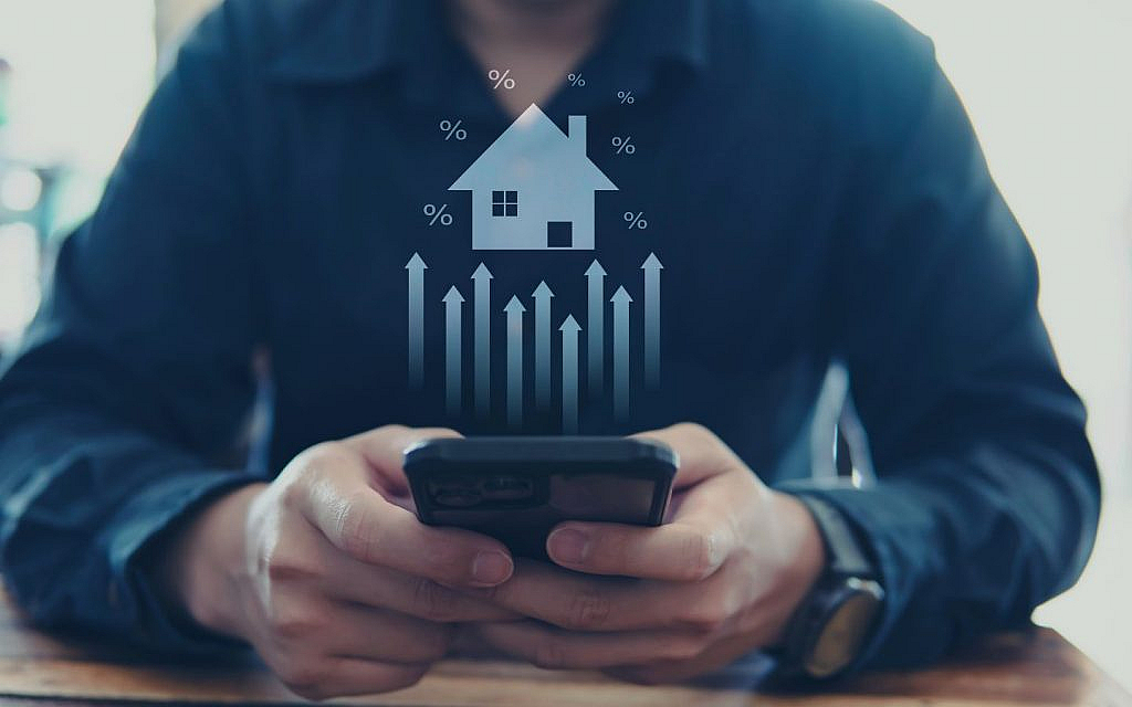 Man using a smartphone with an overlaid image of a house, percentage signs and upward-pointing arrows