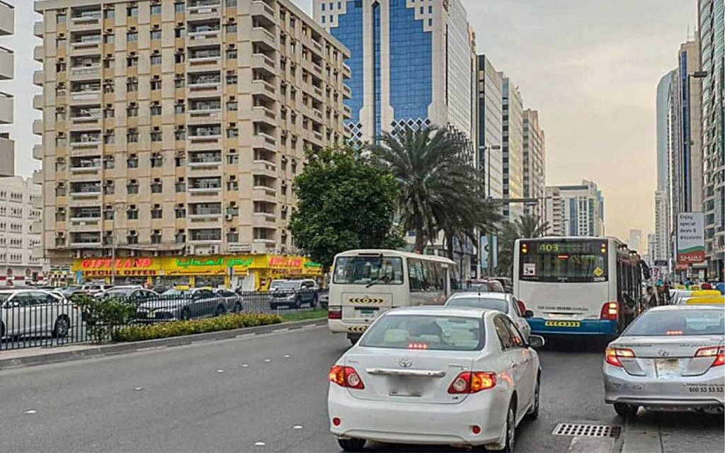 Cars and buses on a busy Hamdan Street in Abu Dhabi, with buildings and palm trees.