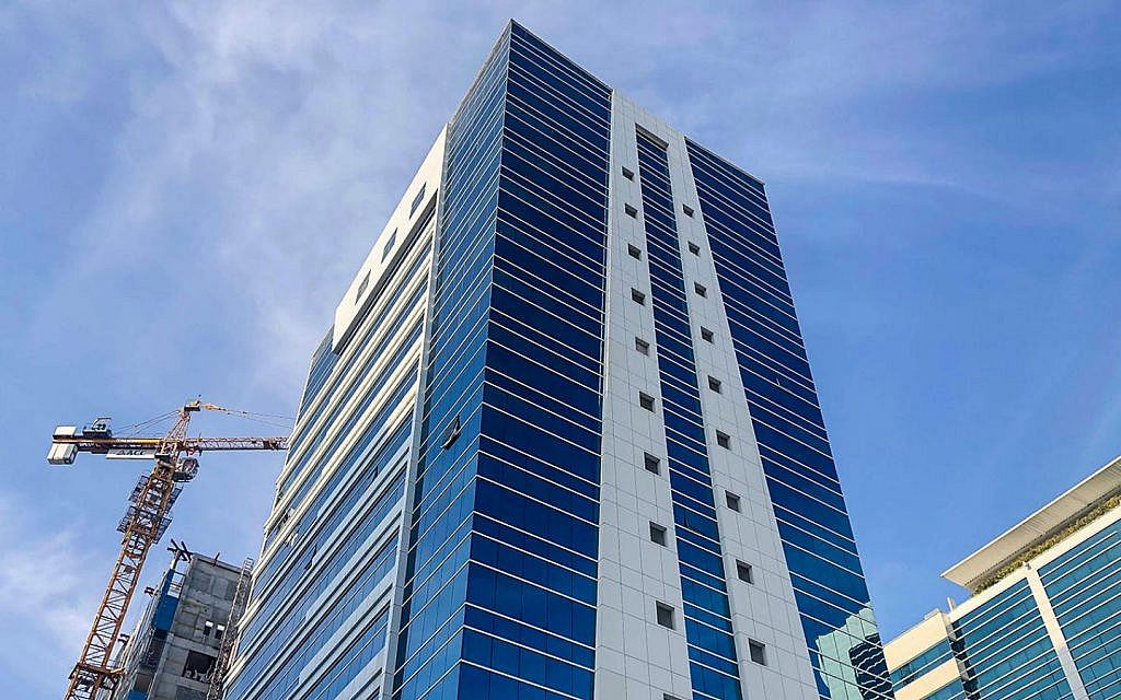 A modern high-rise building with blue glass and white panels against a blue sky, with a construction crane visible