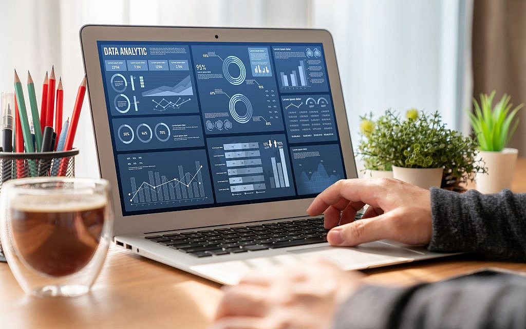 Person typing on a laptop displaying various data analytics dashboards and charts.
