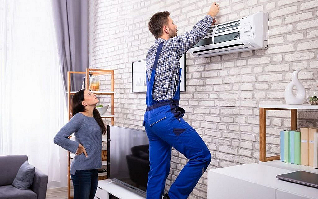 Woman observing a technician servicing an air conditioner on a brick wall.
