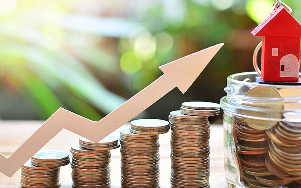 Rising arrow over stacks of coins, with a miniature red house on a jar of coins in the background.
