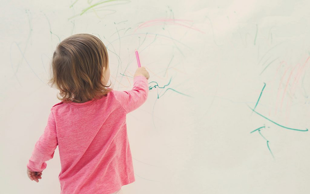 طفلة ترسم بألوان على جدار أبيض