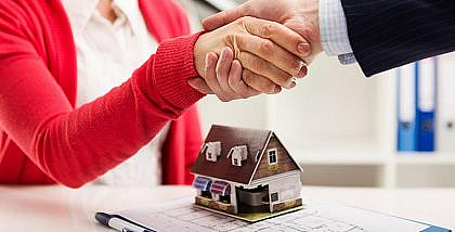 مجسم منزل فوق مخطط عقاري وشخصان يتصافحان