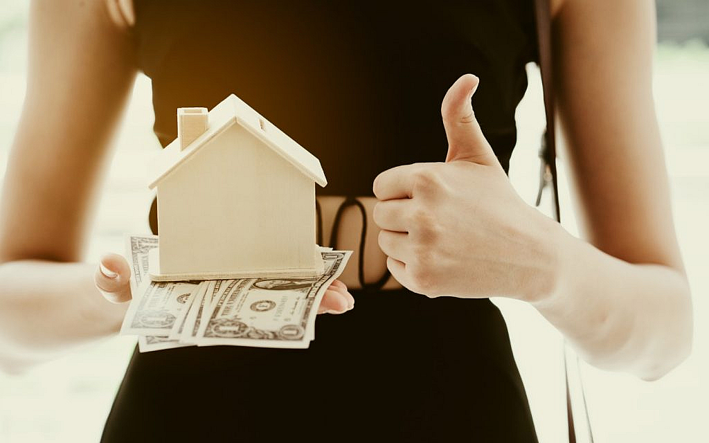 امرأة تحمل مجسم منزل وأوراق نقدية