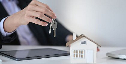 شخص يحمل مفتاح منزل وبجابه مجسم منزل