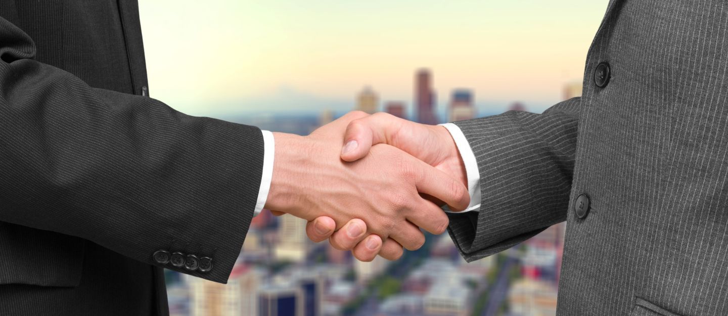Business professionals shaking hands against a city backdrop.