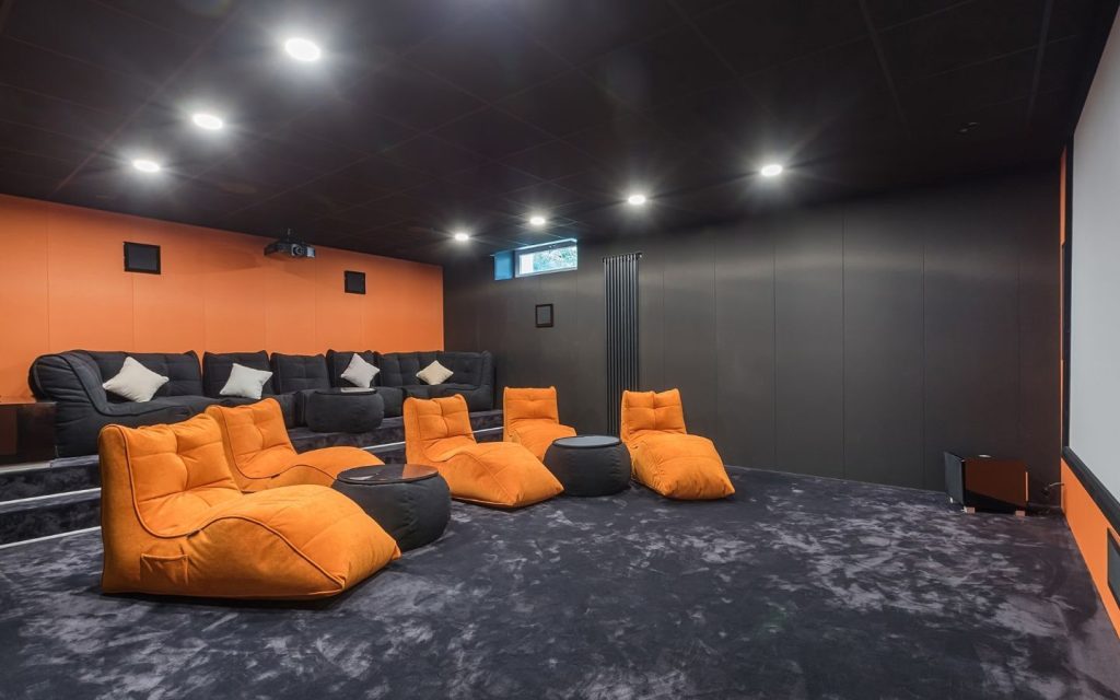 Modern home theatre featuring vibrant orange lounge seating, black walls and a large projection screen.