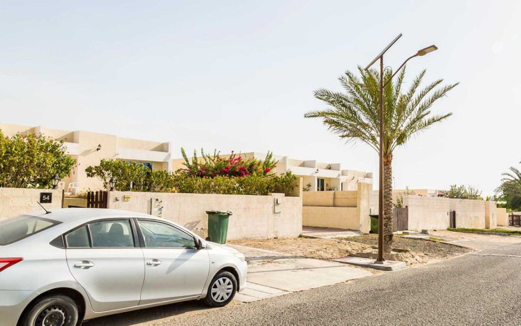 A sedan parked on a quiet residential street lined with white villas and palm trees in Ghantoot.