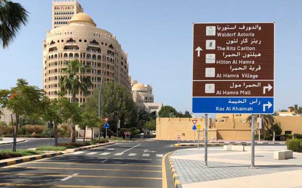 A large brown and blue road sign in Al Hamra Village.