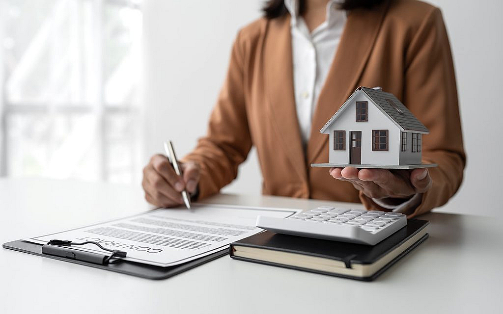 a woman holding a dummy house and signing contract
