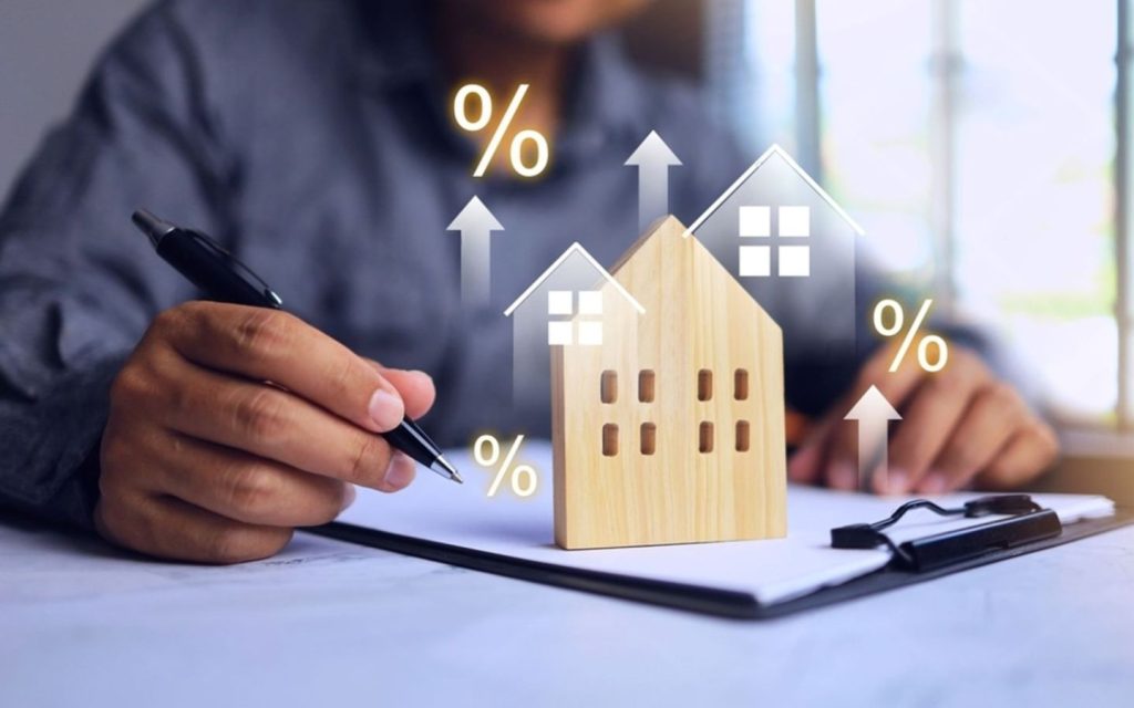 A wooden house model and a hand showing a rent increase